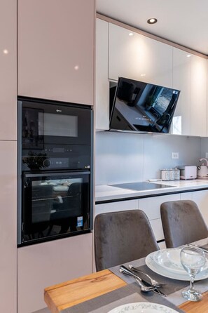 Una cocina moderna con electrodomésticos integrados, un televisor de pantalla plana y un comedor con una mesa preparada para dos personas.