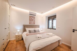 Un dormitorio con cama, mesitas de noche, aire acondicionado, ventana y puerta.