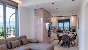 Un salon moderne avec un canapé, un coin repas avec des chaises, une cuisine équipée de meubles et une grande fenêtre offrant une vue dégagée.