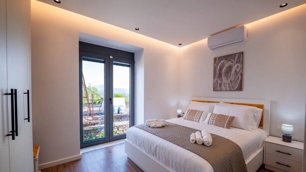 Une chambre moderne avec un grand lit, une porte-fenêtre coulissante donnant sur un balcon et un climatiseur fixé au mur.