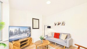 A living room with a flat-screen TV, a grey sofa, a wooden coffee table, and a floor lamp.