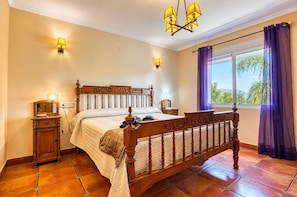 A bedroom with a wooden bed, bedside lamps, a nightstand, and a window with curtains. - Villa 'Emilio' with Sea View, Private Pool and Wi-Fi (Alicante)