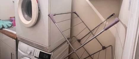 A compact laundry area with stacked washers and dryers, a metal drying rack, and a cabinet above.