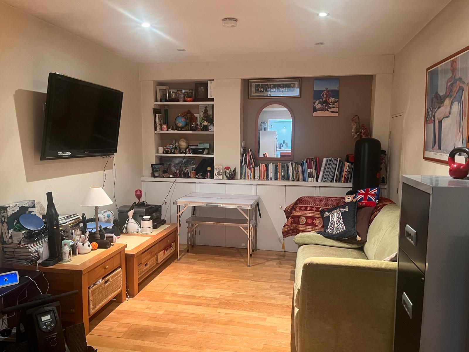 Una sala de estar con un televisor de pantalla plana, una mesa de centro, un sofá y una mesita con varios objetos.