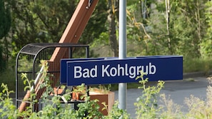 Kadunvarsikyltti, jossa lukee »Bad Kohlgrub», ja sen edessä metalliaita sekä ruukuissa olevia kasveja.
