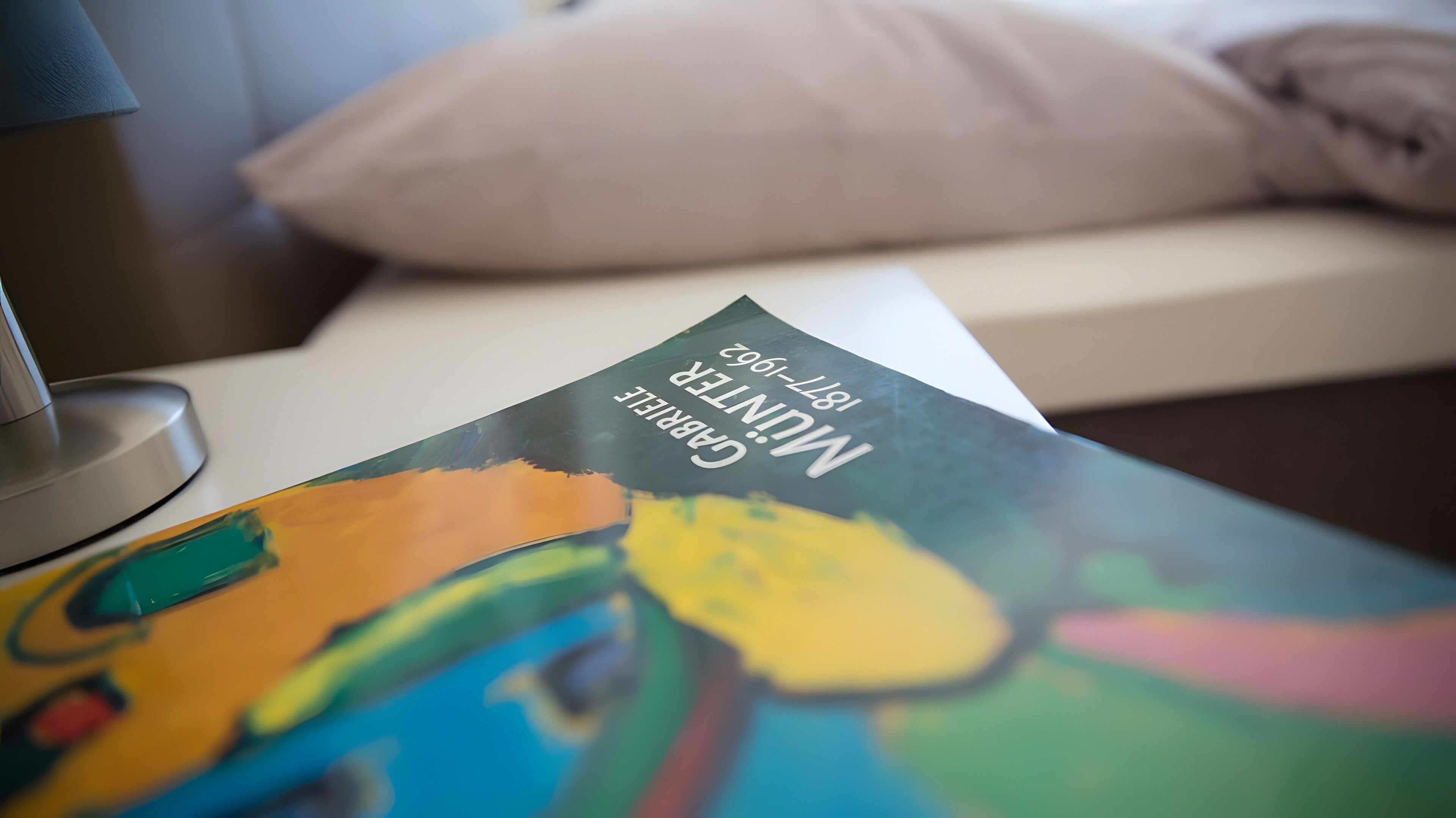 Een boek met de titel 'MUNTER' op een tafel met een kleurrijk abstract schilderij.