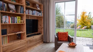 A living room with a wooden bookshelf, a flat-screen TV, a sofa, and a coffee table with a bowl of oranges. - Apartment for 6 Guests (88 m²) in Bad Kohlgrub (Bad Kohlgrub)