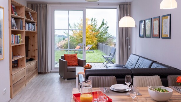 A modern living room with a sofa, dining table, and a bookshelf. - Apartment for 6 Guests (88 m²) in Bad Kohlgrub (Bad Kohlgrub)