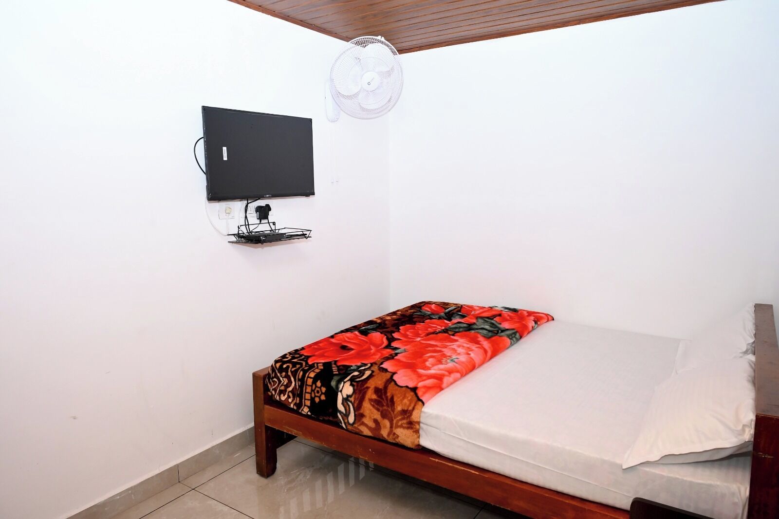 A small room with a bed, a wall-mounted TV, and a ceiling fan.