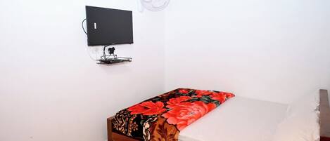 A small room with a bed, a wall-mounted TV, and a ceiling fan.