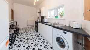 A compact kitchen with a star-patterned floor, a washing machine, a toaster, and a window with plants. - Free Parking Sleeps 2 Central Location (Reading)