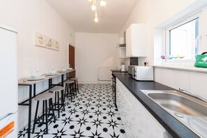 A kitchen with a black and white star-patterned floor, a long counter with stools, a sink, and a window with a bag on the sill. - Free Parking Sleeps 2 Central Location (Reading)
