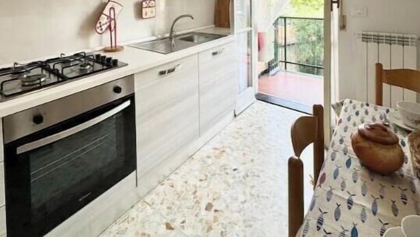 Una cocina moderna con estufa a gas, horno y pileta. Hay una mesa de comedor con sillas y vista al exterior a través de un ventanal.