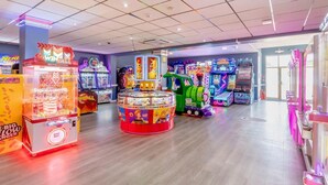Un salón de juegos muy iluminado con diversas máquinas, incluyendo máquinas de garra y de carreras.