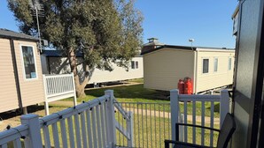 Una terraza con baranda blanca, una silla negra y vista a casas móviles al fondo.