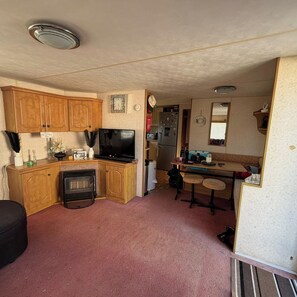 A compact kitchen with wooden cabinets, a stove, a refrigerator, and a small dining area with stools.