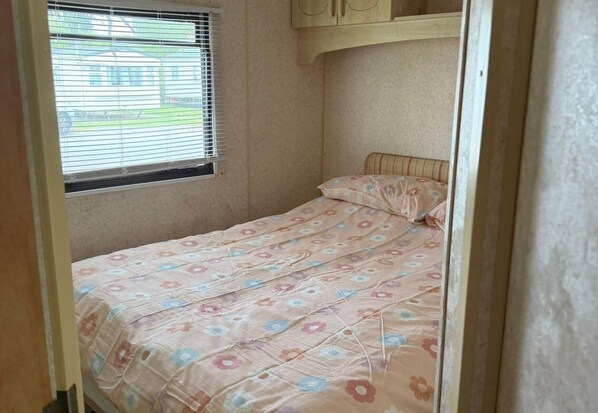 Une petite chambre avec un lit simple, une fenêtre avec des stores et une porte.