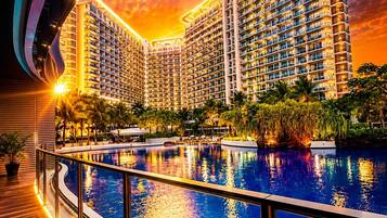 Un hotel moderno alto con piscina, rodeado de vegetación y un cielo al atardecer.