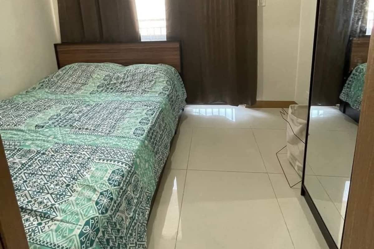 A bedroom with a bed, an air conditioner, a window with curtains, and a mirror.