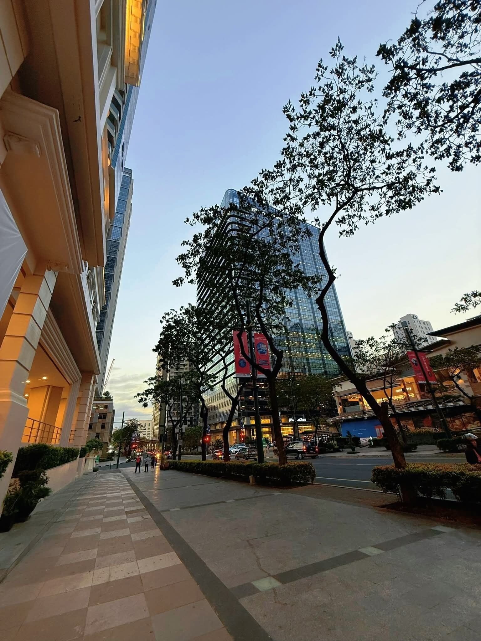 A city street with modern buildings, a clear sky, and a pedestrian walkway.