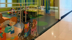 A daycare center with a play area, a large glass window, and a ceiling fan. - Her Casa Stays (Paranaque)