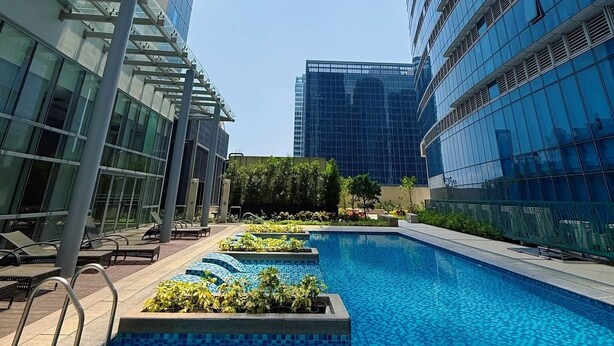 A swimming pool with a tiled deck, surrounded by modern buildings with reflective glass facades. - Her Casa Stays (Paranaque)