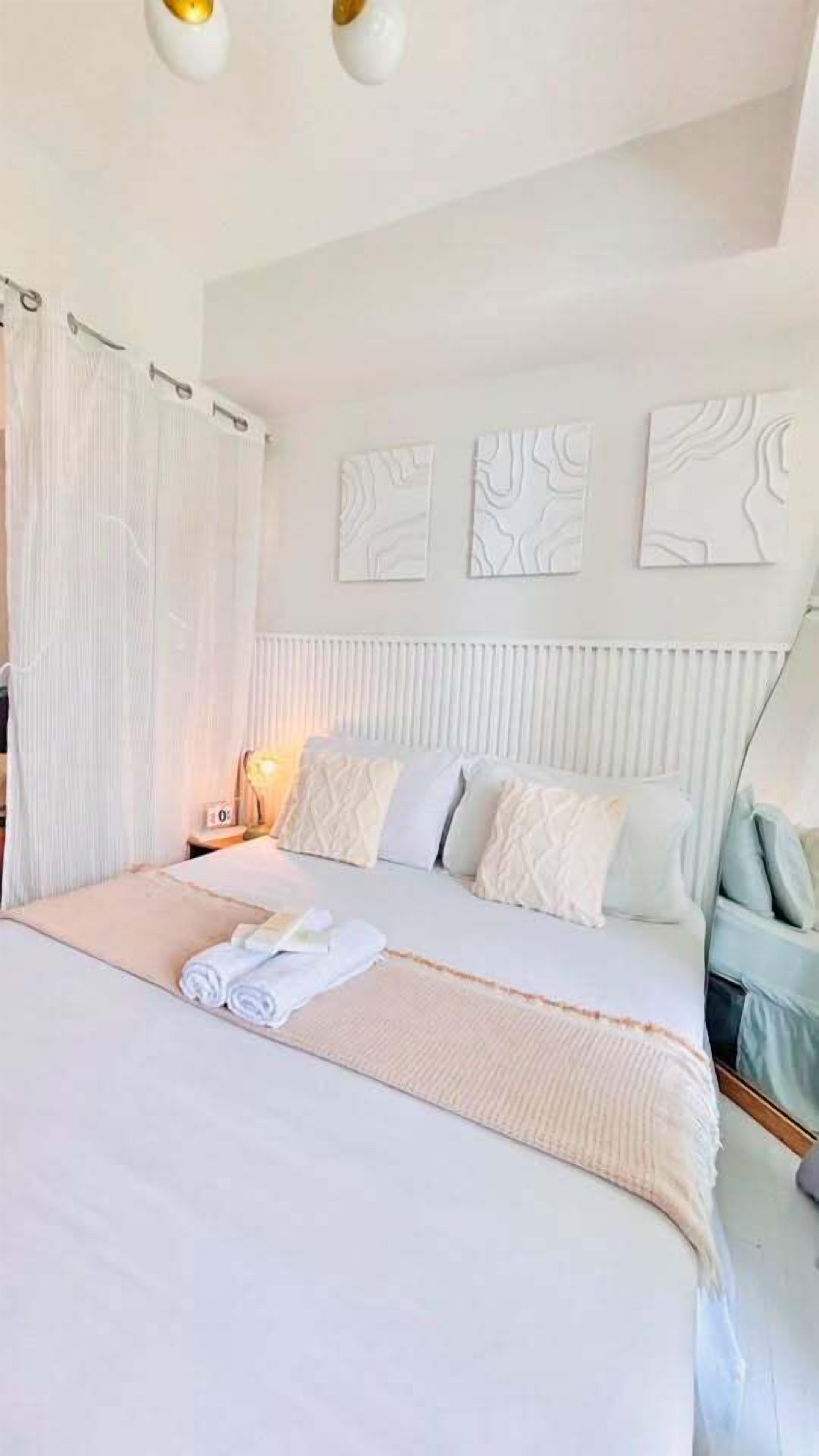 A bedroom with a large bed, a nightstand, a lamp, and a window with curtains.