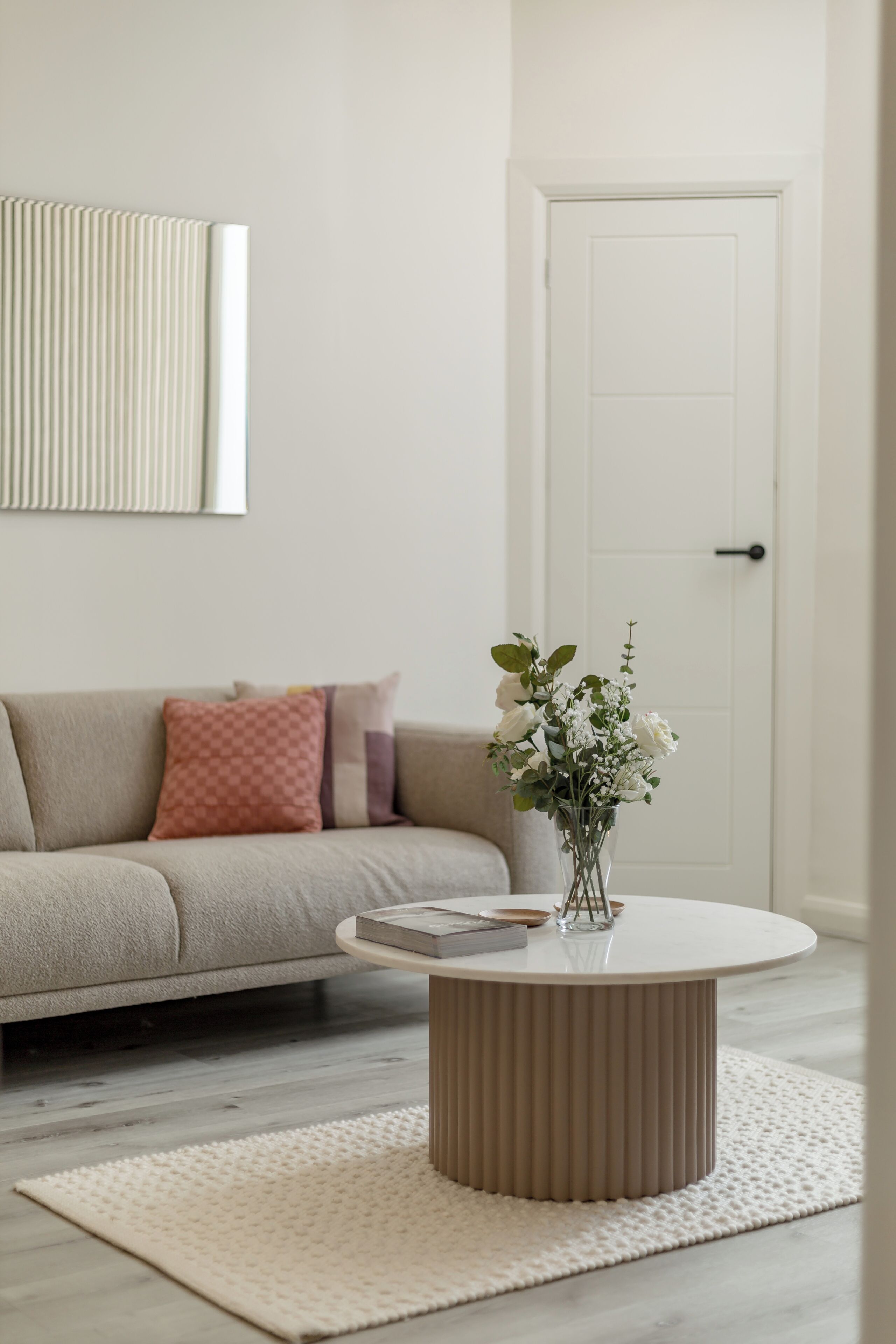 A living room with a beige sofa, a round coffee table, and a white door in the background.