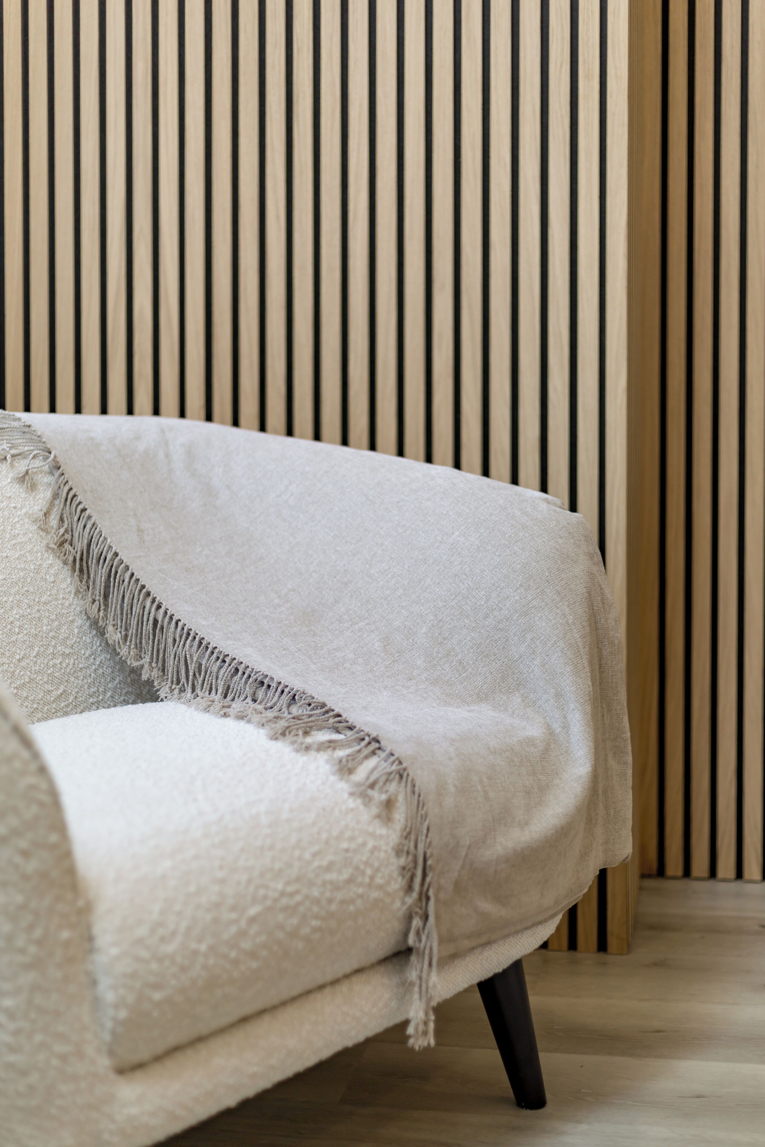 A sofa with a textured cover and a fringe detail, positioned against a wall with vertical wooden slats.