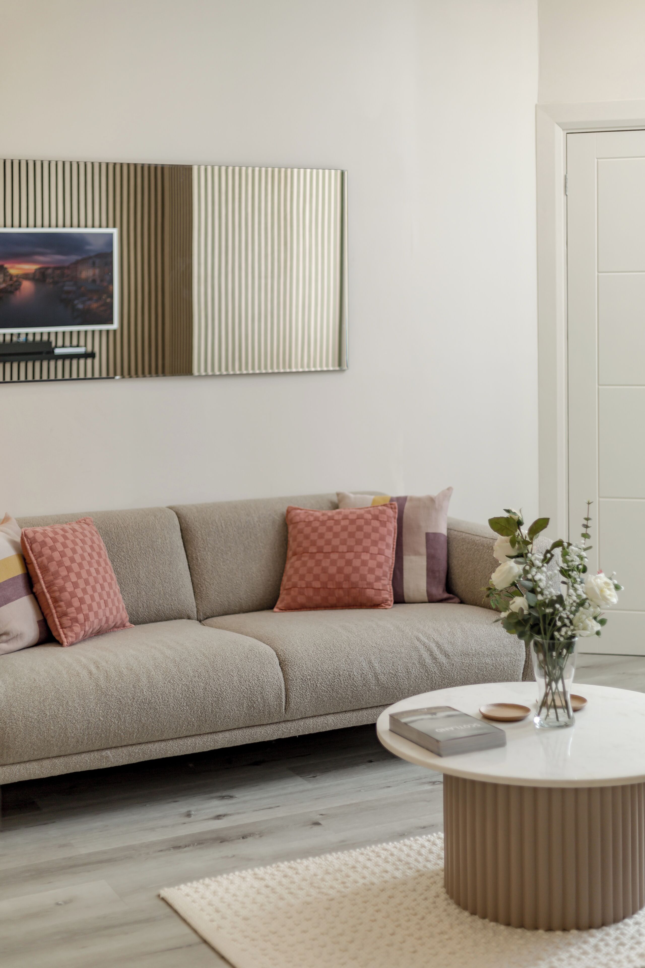 Un salon comprenant un canapé, une table basse ronde, un téléviseur fixé au mur et une porte.