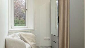 Un dormitorio con ventana, armario, silla y alfombra redonda.
