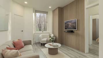 Una sala de estar moderna con un sofá, una mesa de centro, un televisor montado en una pared de paneles de madera y una ventana con vistas a árboles.
