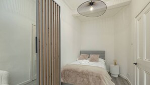 Un dormitorio con cama, mesita de noche, lámpara y puerta.