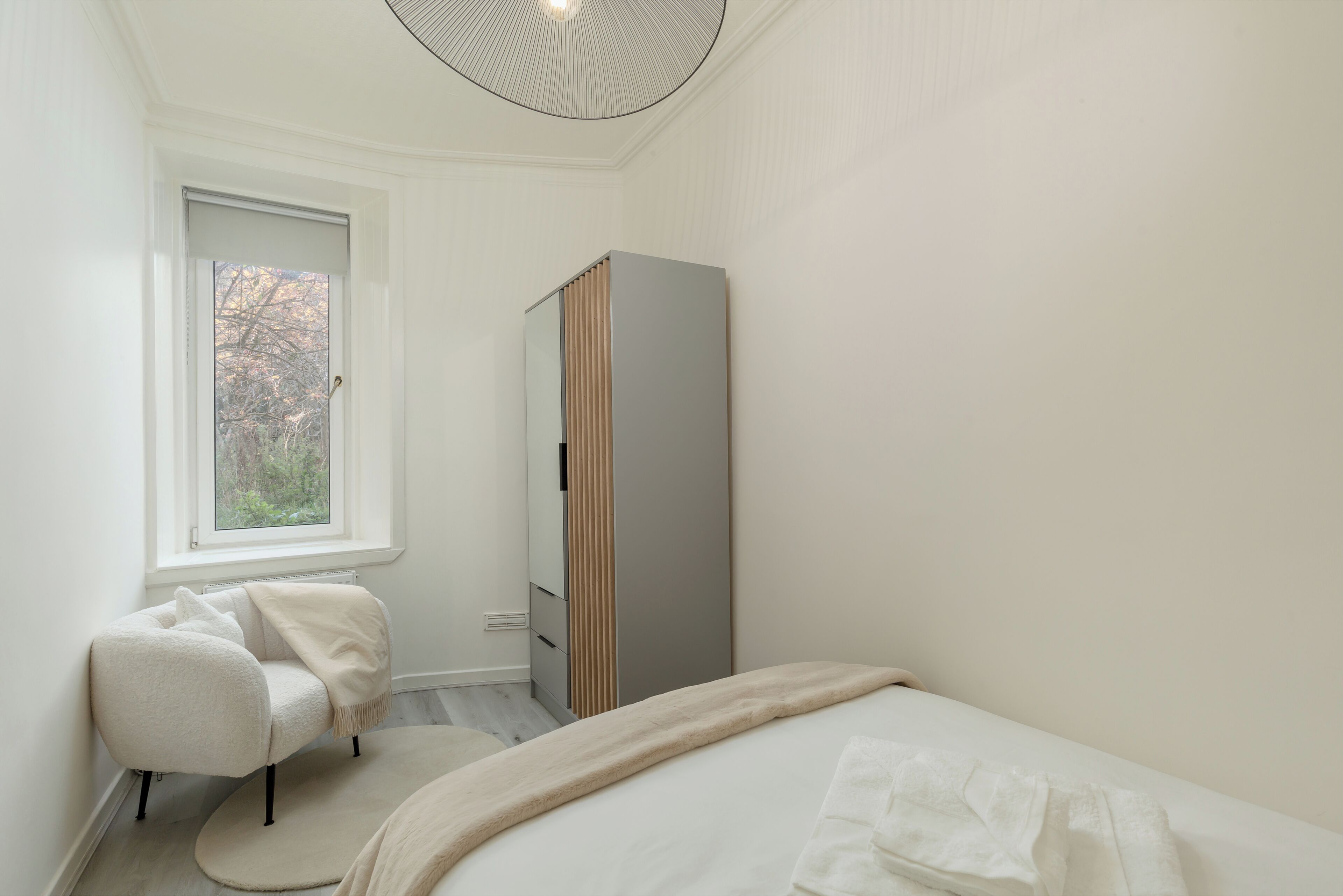 A bedroom with a bed, a chair, a wardrobe, a window, and a radiator.