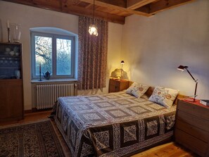 Ein Schlafzimmer mit Bett, Fenster, Heizkörper, Nachttisch mit Lampe und einem Schminktisch.