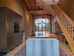 Eine moderne Küche mit einer zentralen Kochinsel, einer Holztreppe und großen Fenstern.