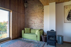 Ein Zimmer mit einem grünen Sofa, einem Kamin, einem gemusterten Teppich und Blick durch ein Fenster.