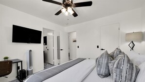 Une chambre d’hôtel moderne équipée d’un lit, d’un ventilateur de plafond, d’un téléviseur à écran plat, d’un bureau avec une chaise et d’une lampe de chevet.