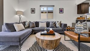 Un salon moderne avec un canapé d’angle, une table basse ronde et une vue sur la cuisine.