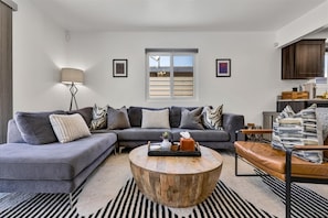 Ein modernes Wohnzimmer mit einem Ecksofa, einem runden Couchtisch und Blick zur Küche.