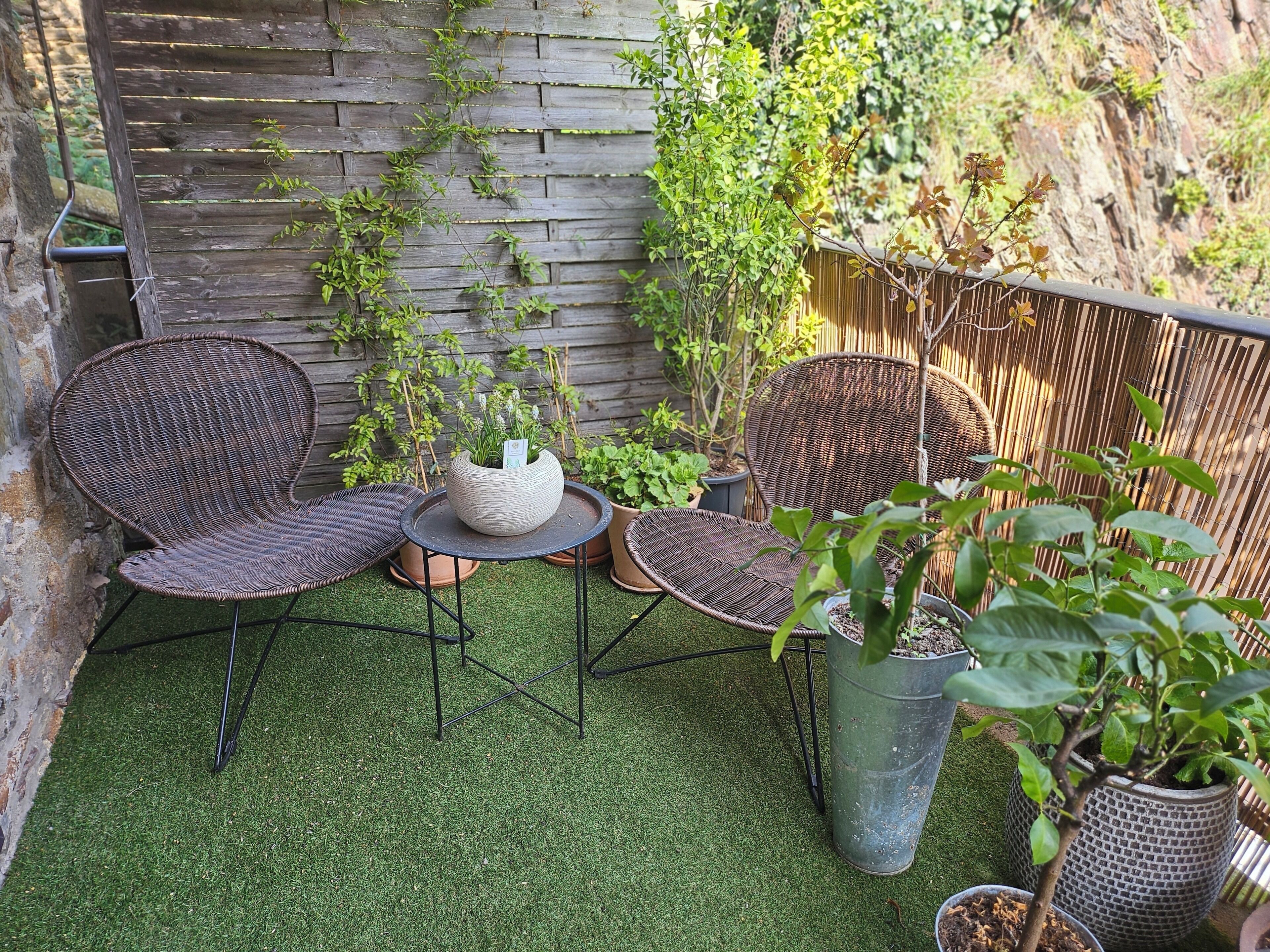 A patio with two wicker chairs, a small table, and potted plants.