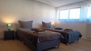 Ein Schlafzimmer mit zwei Betten, Nachttischen und einem Fenster mit durchsichtigen Vorhängen.