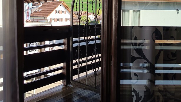 Eine Holzterrasse mit einem Metallzaun, Blick auf Häuser und ein Berg im Hintergrund.