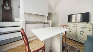 Ett kompakt bostadsutrymme med ett litet kök, en matplats, en tv och en mönstrad matta.