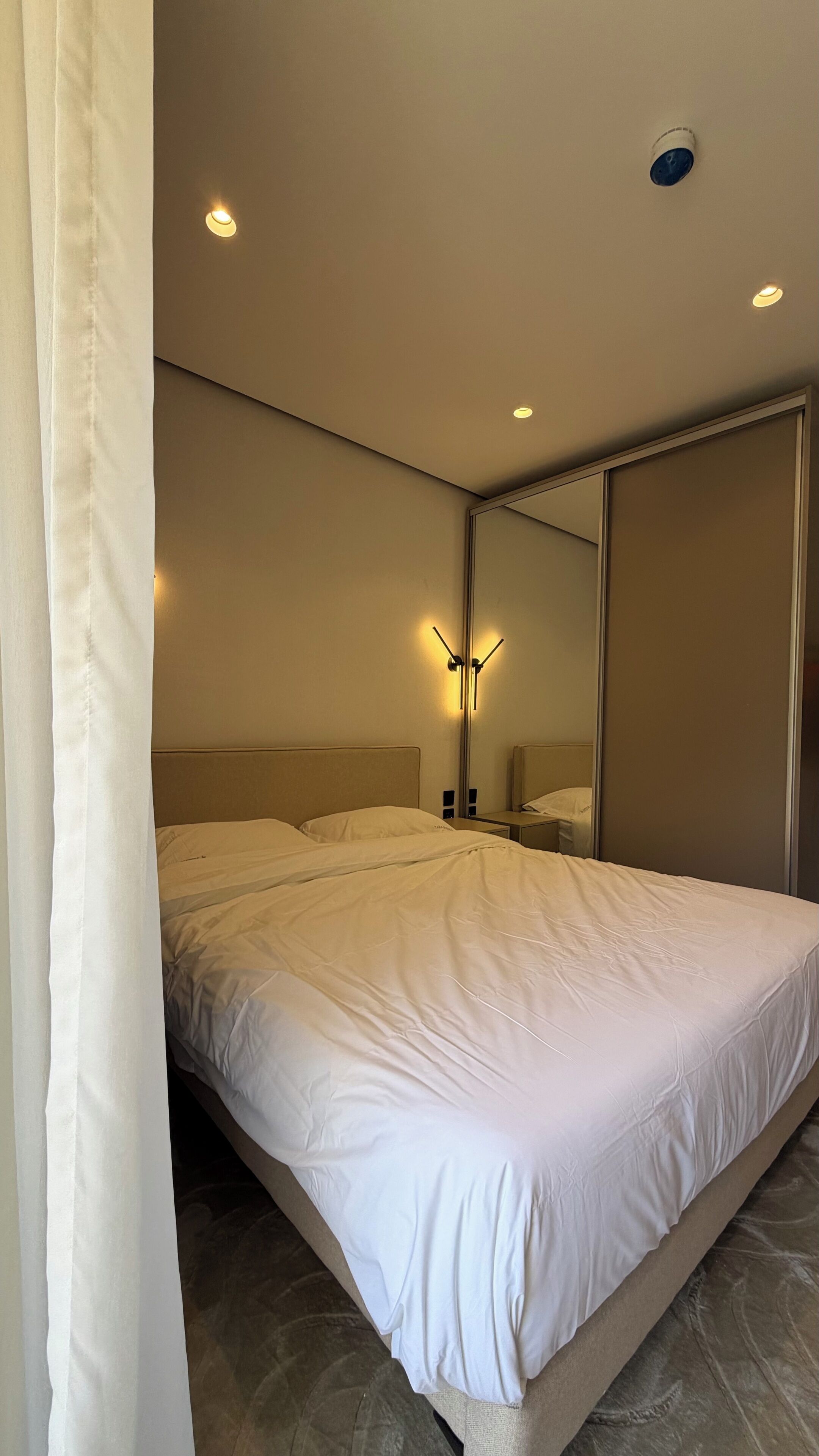 Ein modernes Schlafzimmer mit einem großen Bett, Nachttischlampen, einem Spiegel und Einbauleuchten.