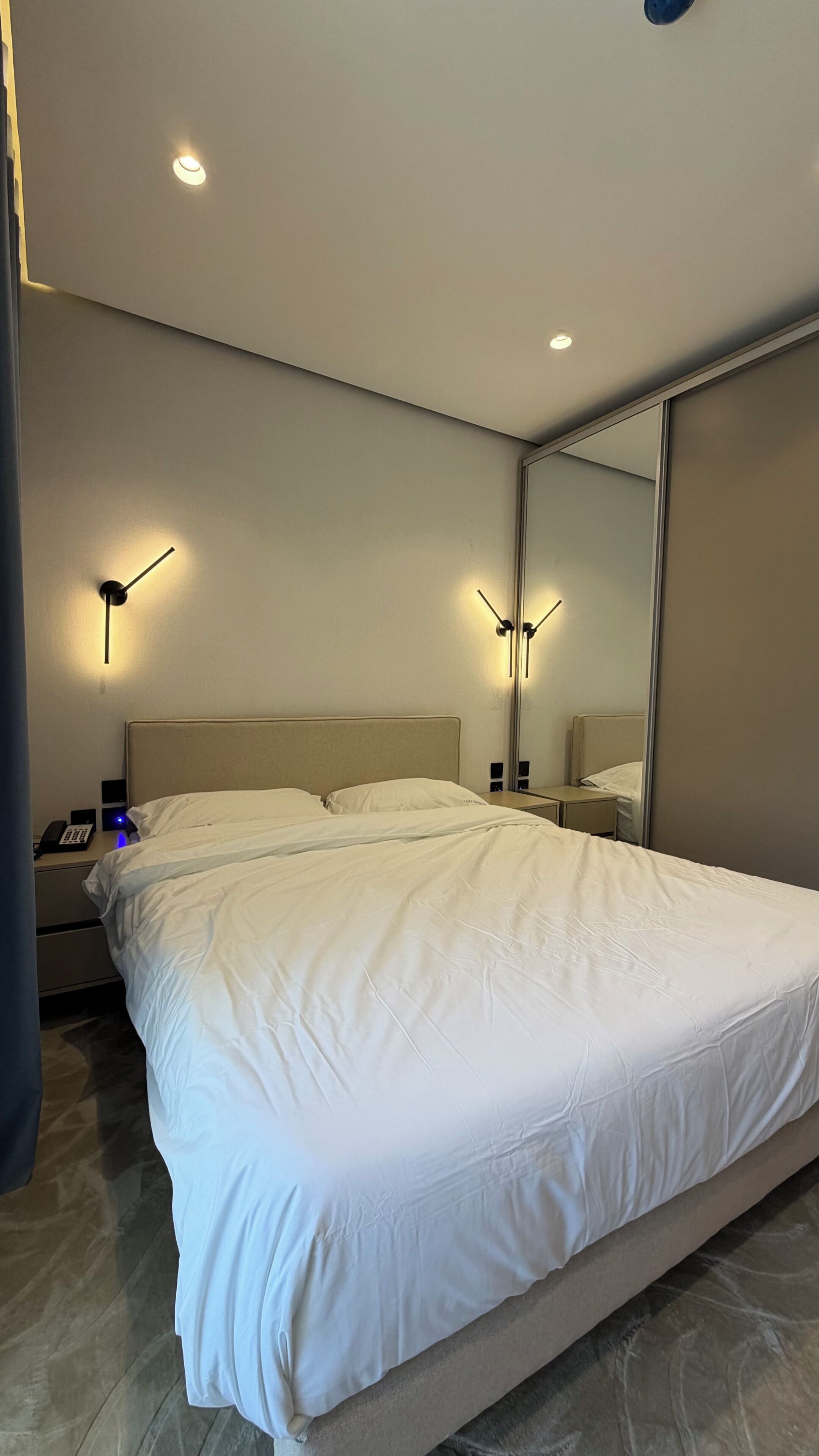 Et moderne hotelværelse med en stor seng, sengeborde, lamper og et spejl.