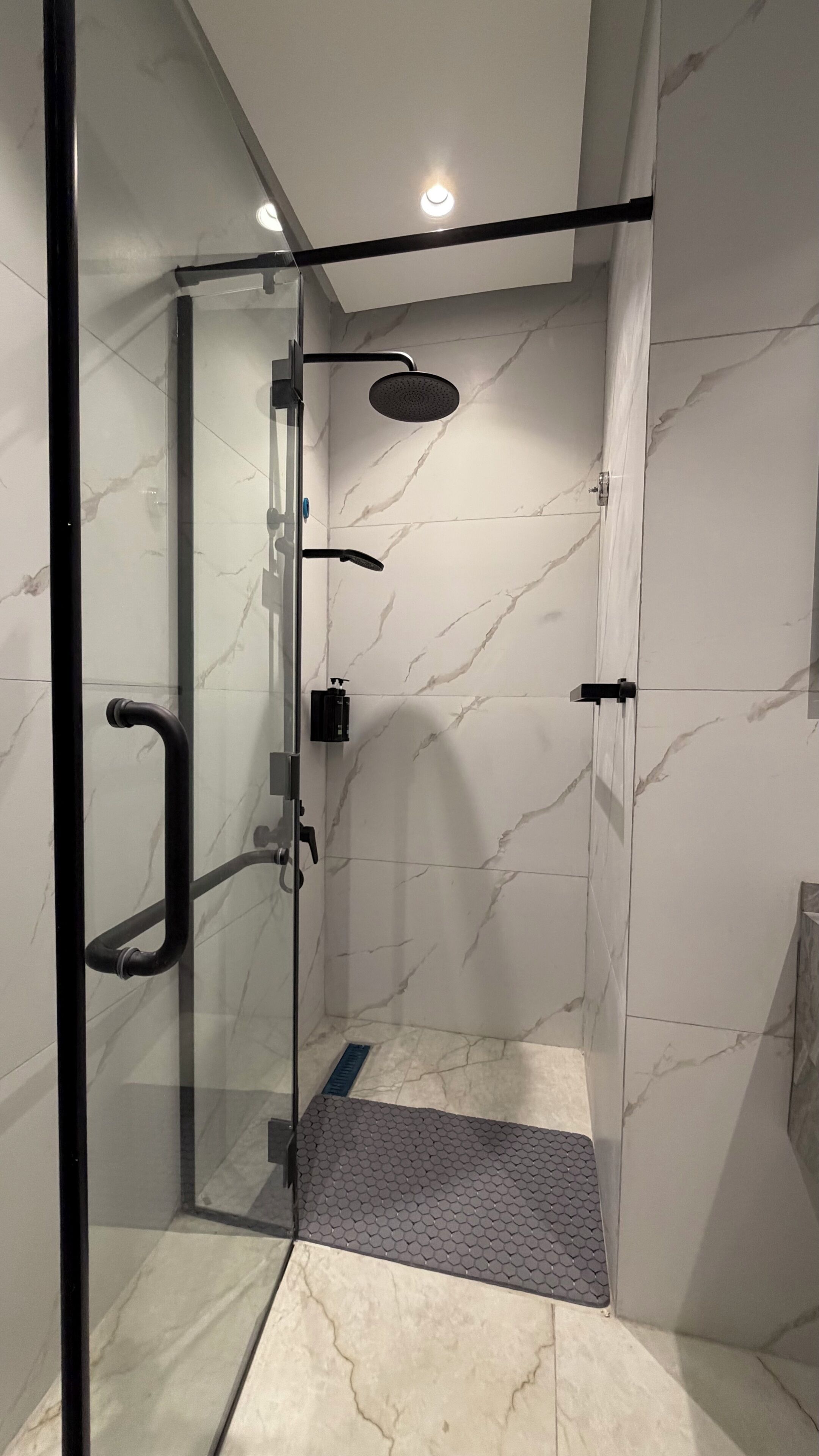 A glass-enclosed shower with a handheld showerhead and a wall-mounted faucet.