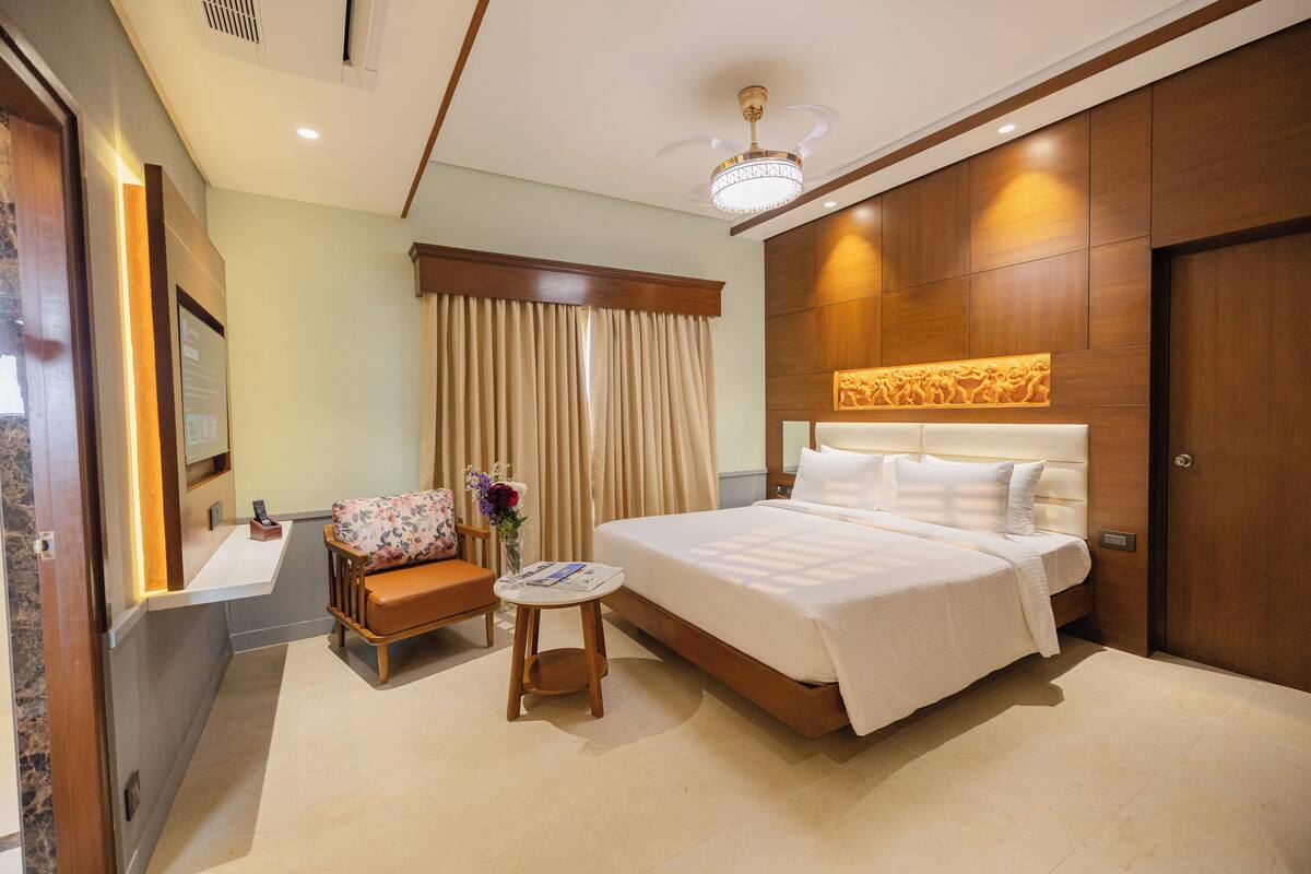 Una habitación de hotel con una cama grande, una mesita, un sofá, un espejo y un cabecero de madera.