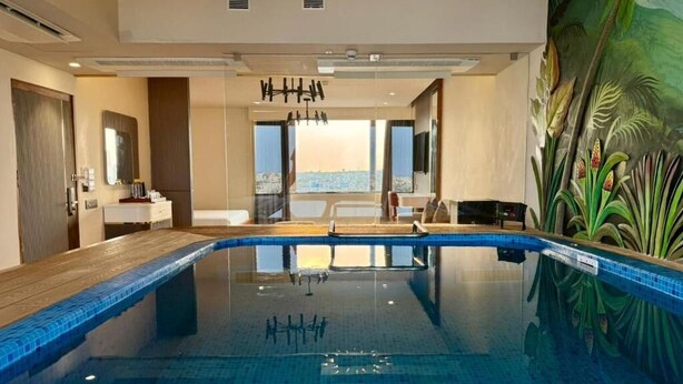 A modern indoor pool with clear glass walls, a wooden deck, and a mural of tropical plants. - SKI - Sivakavi Iconic (Puducherry)