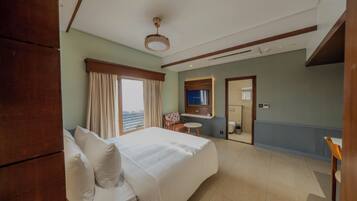 A hotel room with a large bed, a small table, a chair, a mirror, and a view of the city.